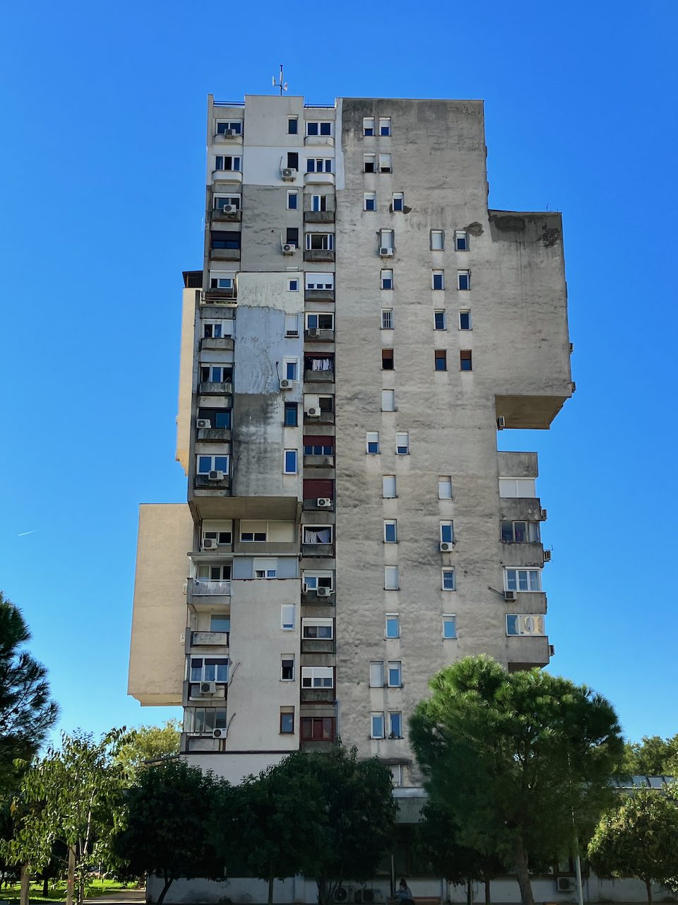 A weathered concrete apartment tower against a clear sky