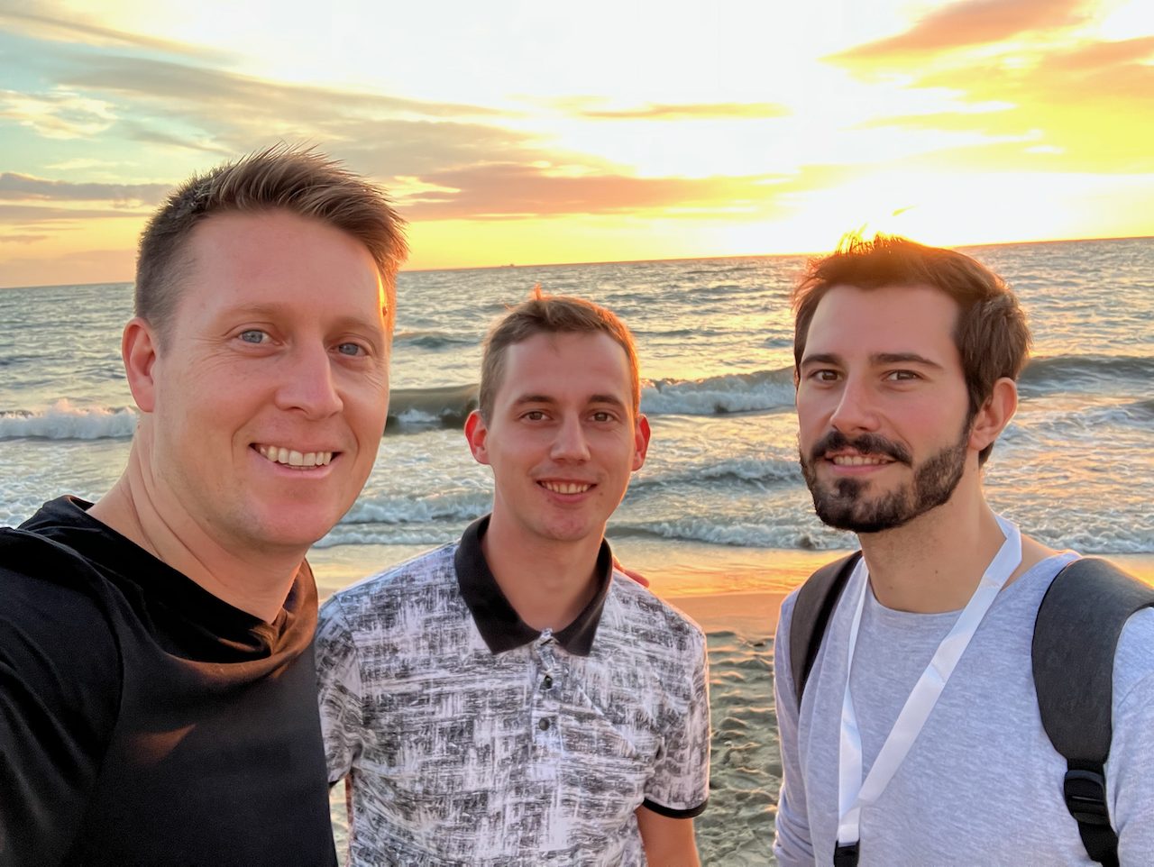 Three men standing together by the sea at sunset