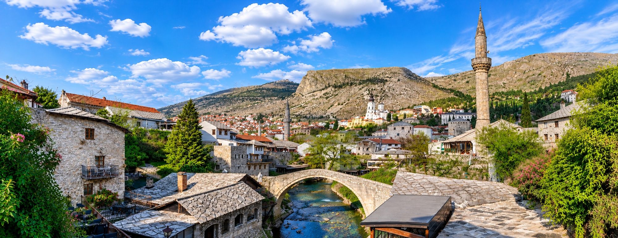A Balkan city of stone rooftops, a minaret and an old bridge beneath the mountains