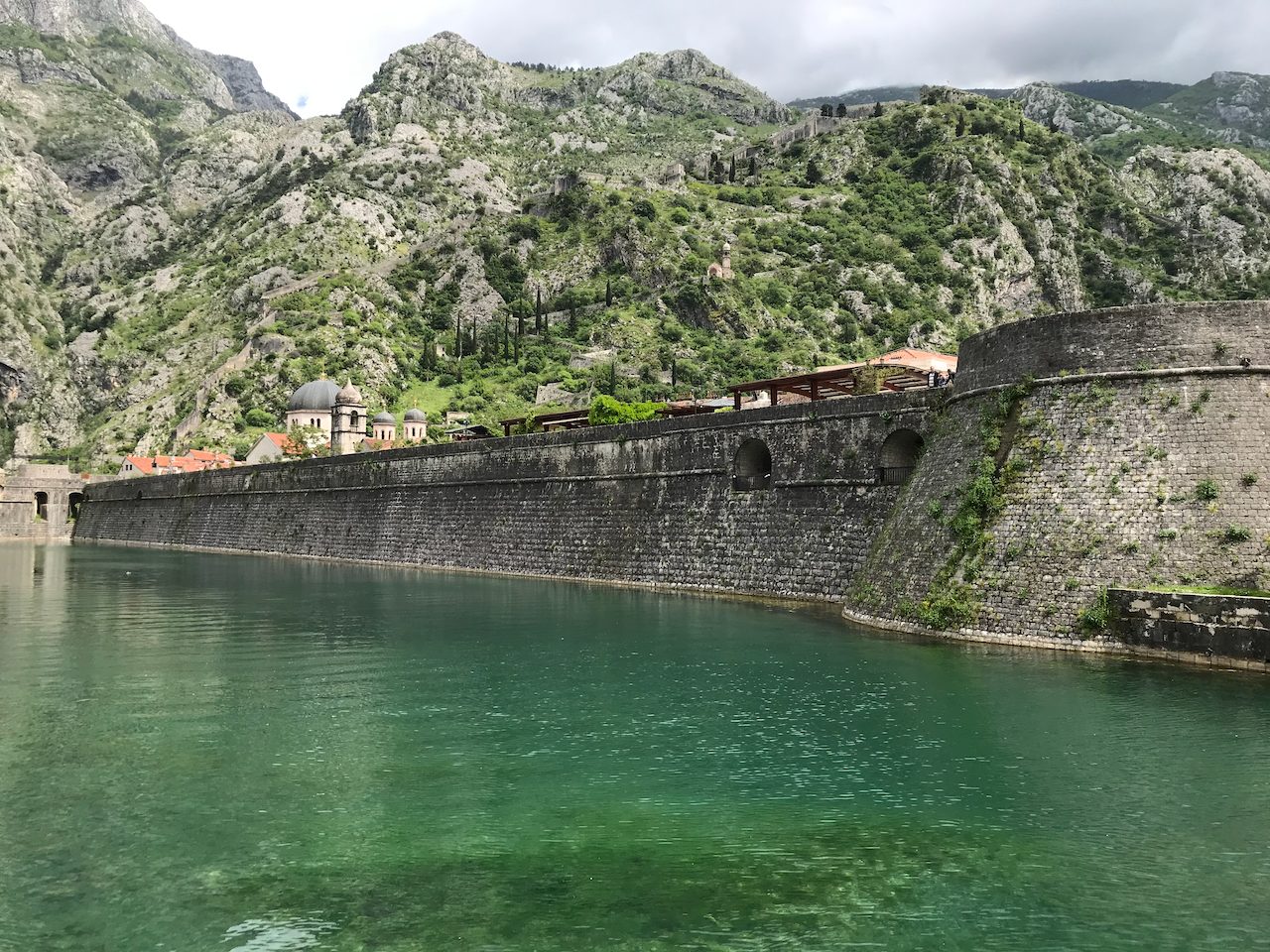 A deep bay ringed by mountains with an old fortress wall climbing the ridge