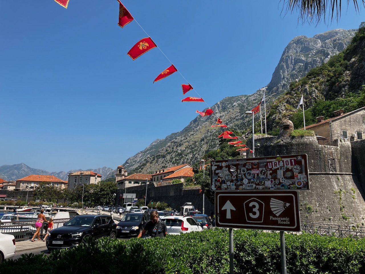 Montenegrin flags strung above a street beneath steep mountains and old fortress walls