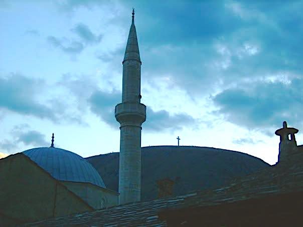 A minaret and a church cross rising side by side against the sky