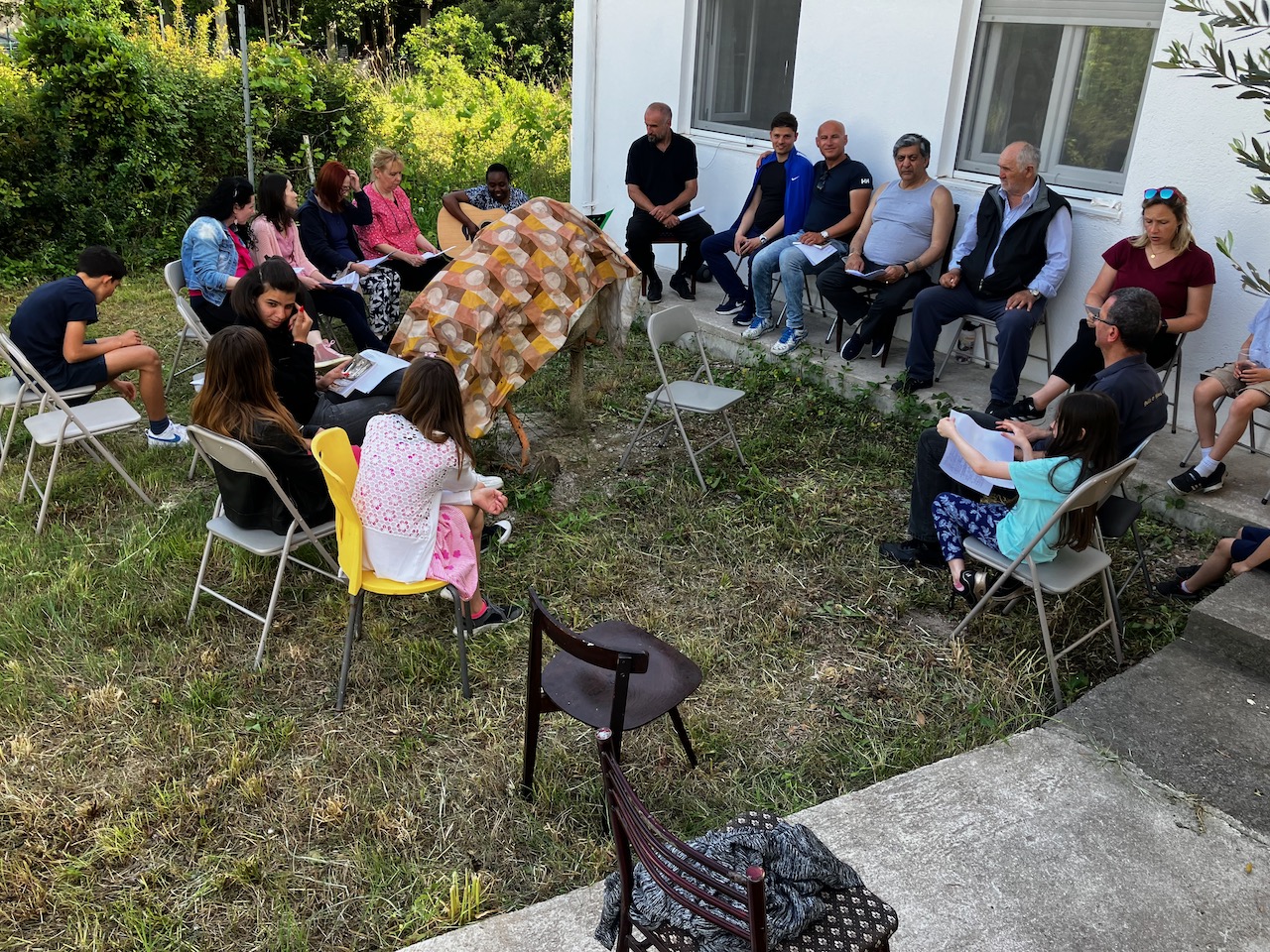 A gathering of families and children seated outdoors in a yard for a time of teaching