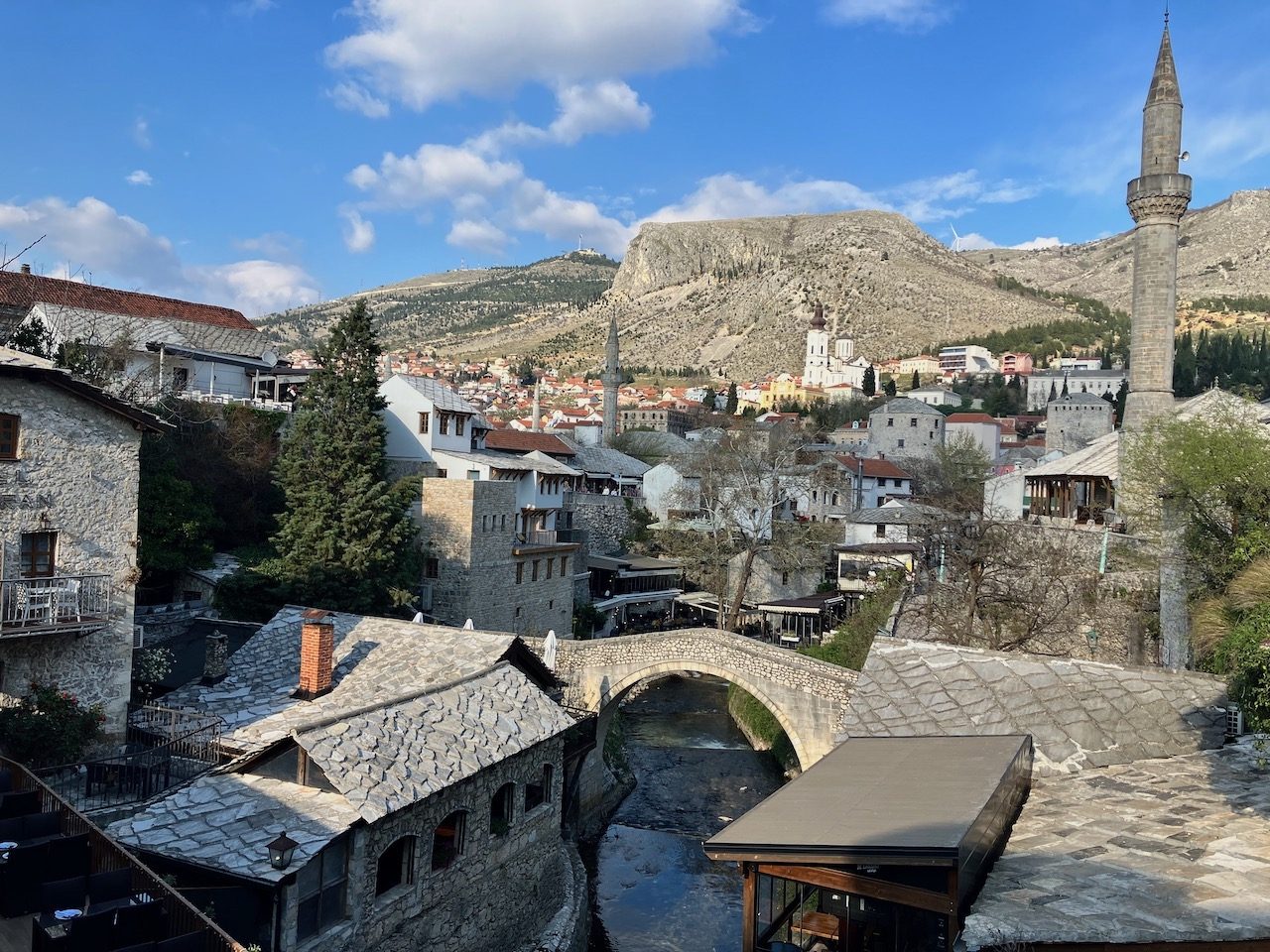 An old stone bridge over a river beside a minaret and stone houses